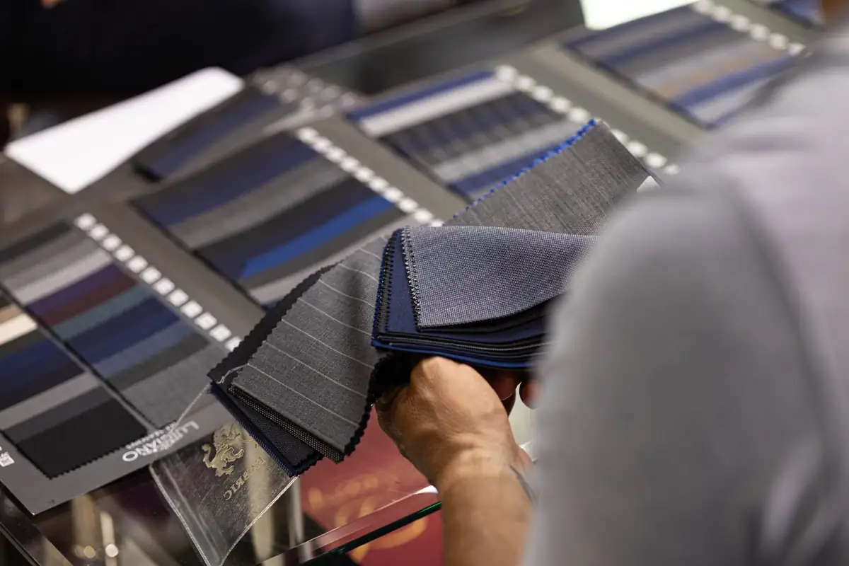 Customer lifting a fan of grey and navy suiting swatches out of a fabric book