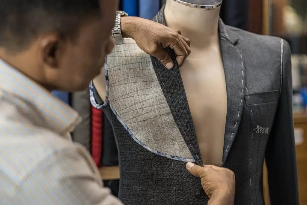 Tailor pinning back the canvassed front of a half-made grey jacket on the dress form