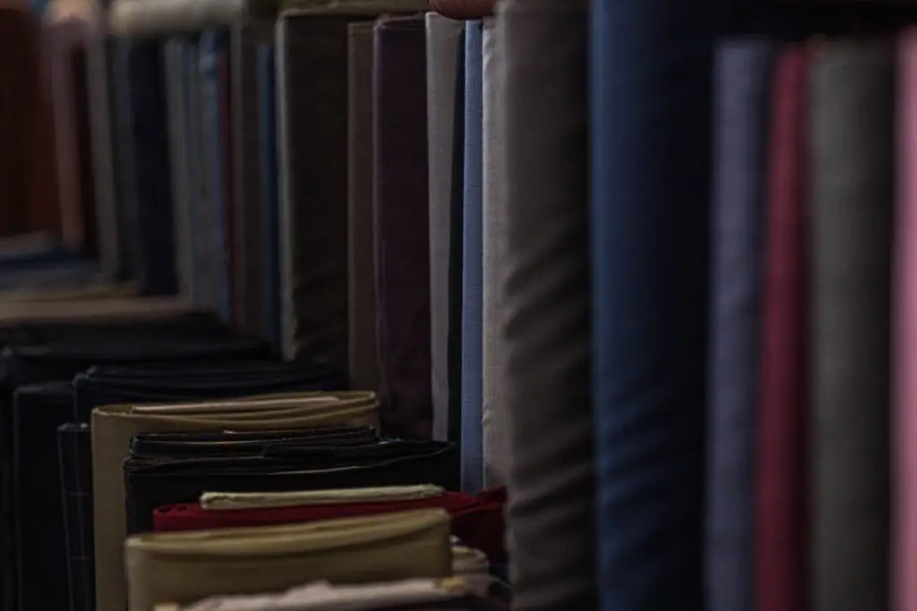 Suit lengths standing on end in the fabric room with folded shirtings stacked in front