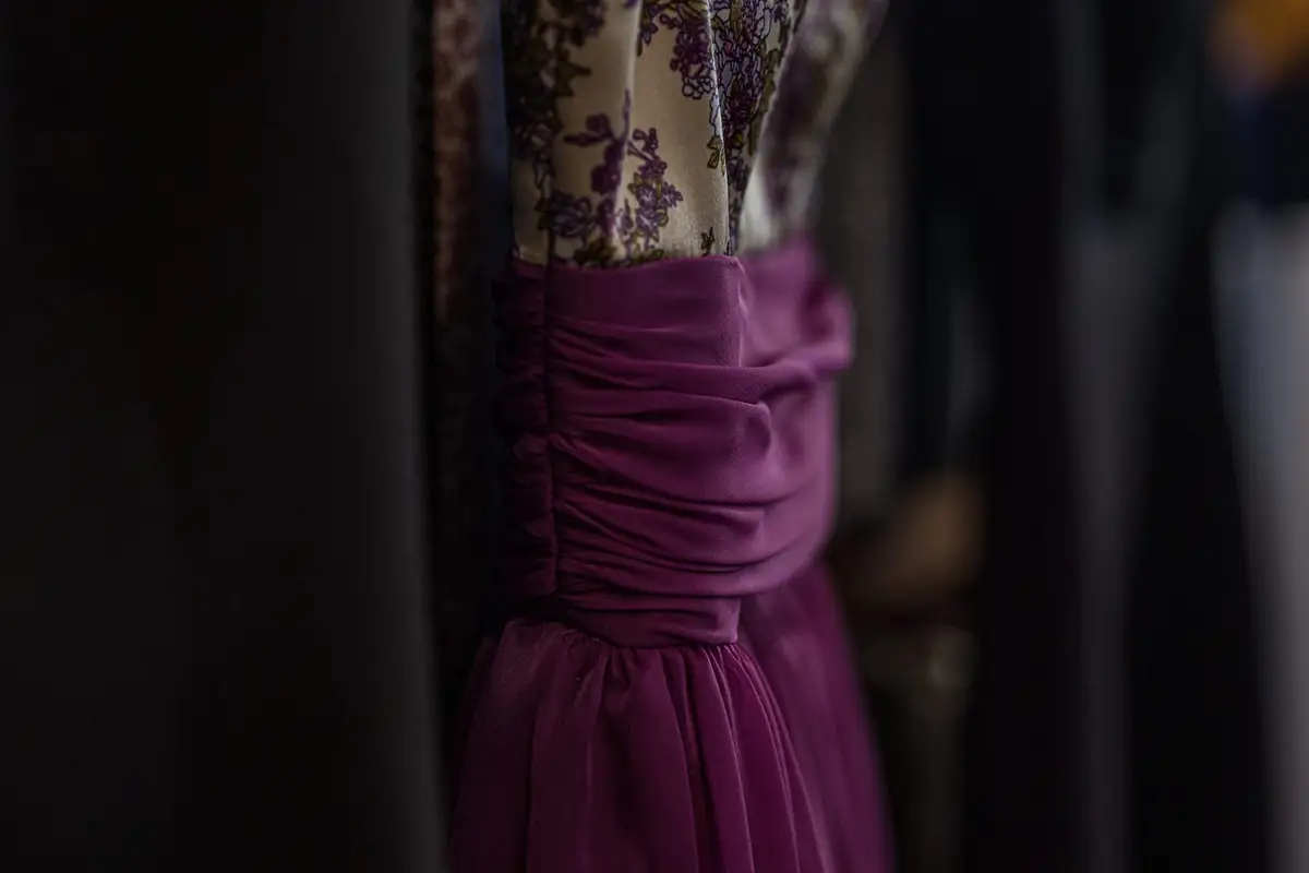 Magenta chiffon evening dress with a ruched waist hanging beside a floral print gown